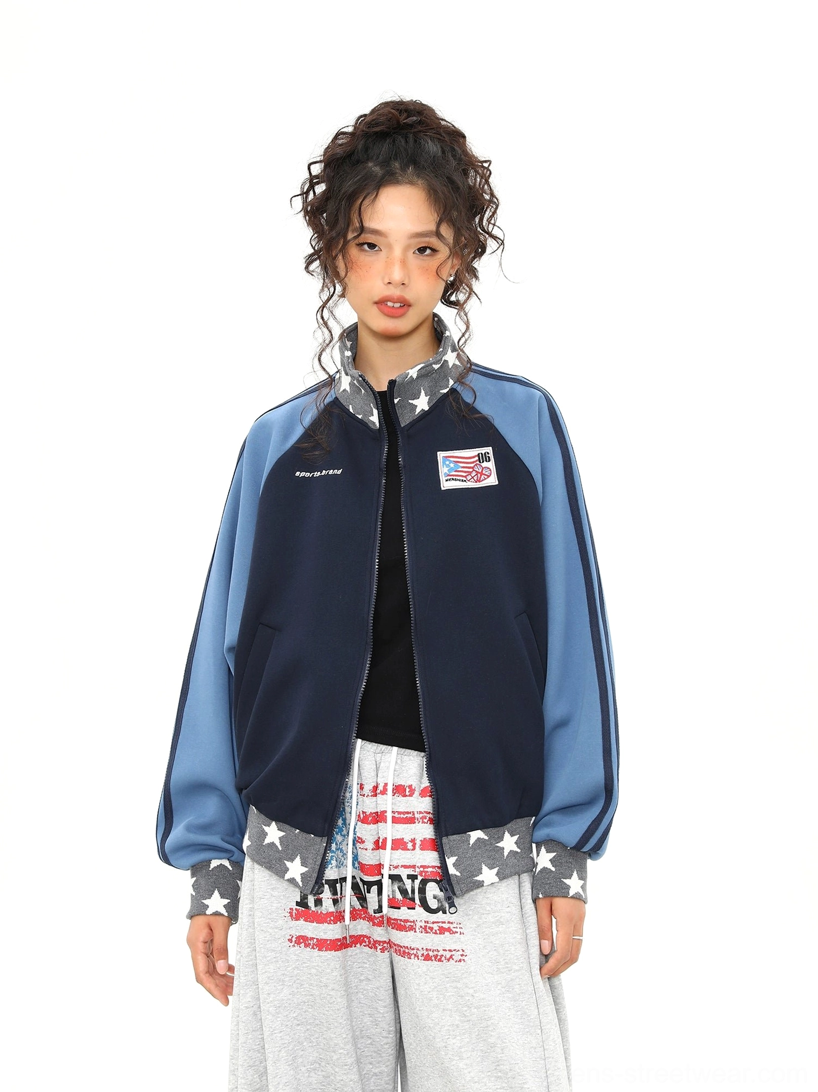Female model wearing an open navy and blue raglan varsity track jacket with star print collar trim in a white studio