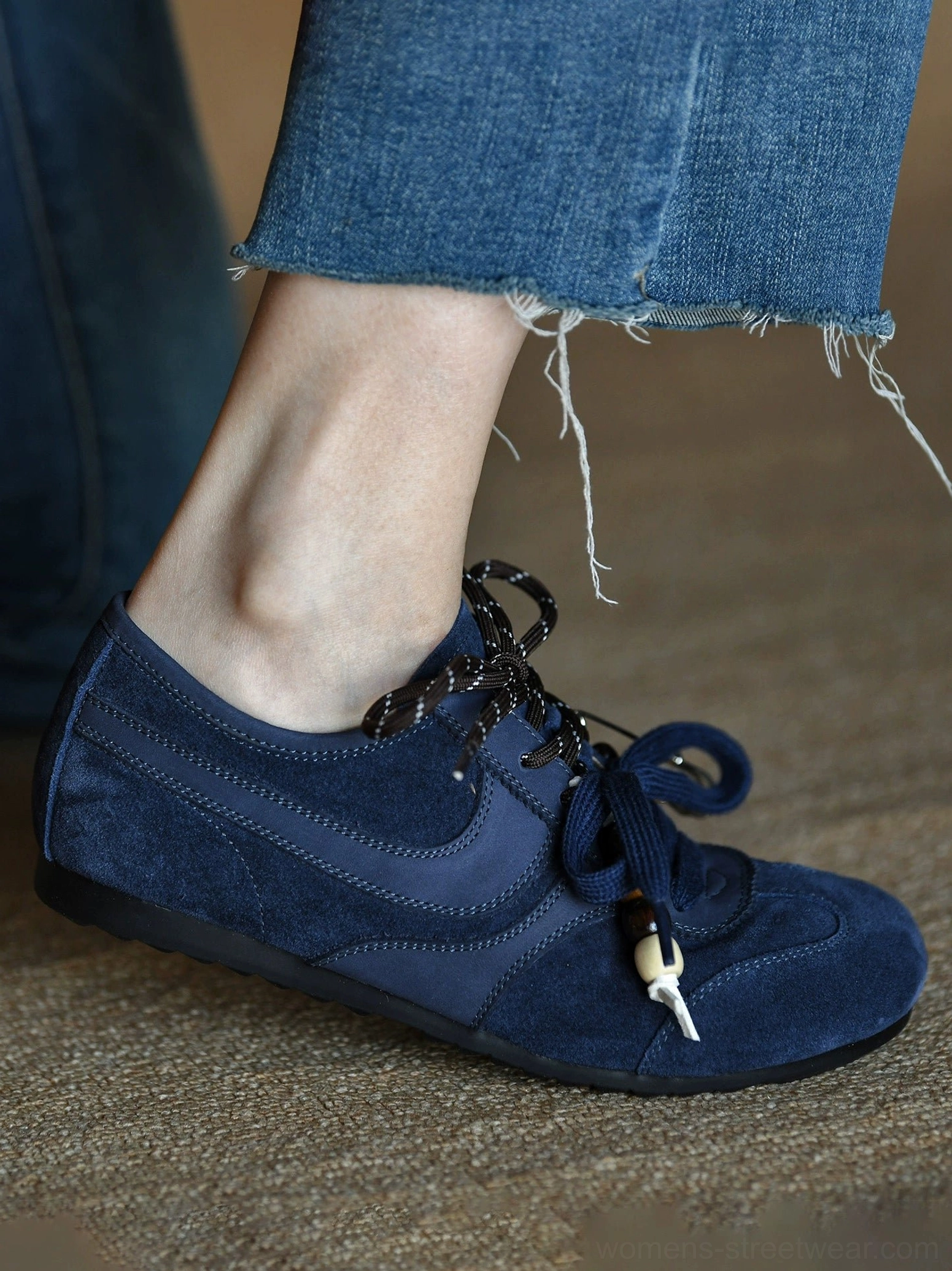 Side profile of a navy blue suede low-top retro sneaker showing curved suede panels and a relaxed ankle opening