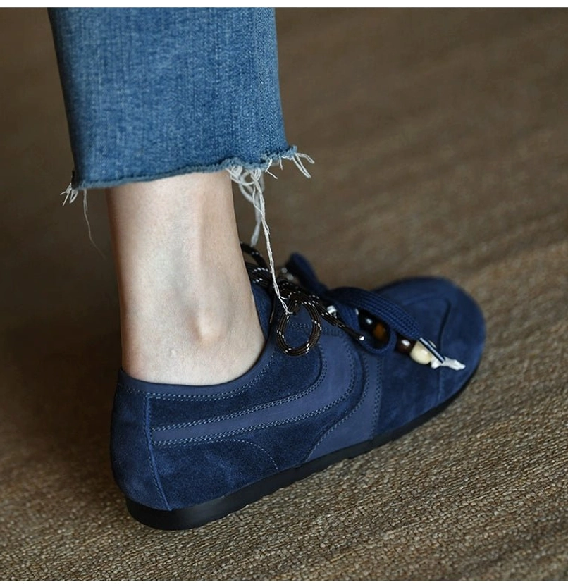 Rear angled view of a navy blue suede low-top sneaker worn with frayed cropped denim and stitched panel details