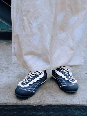 Pair of navy contrast-stitch low-profile trainers worn with off-white wide-leg trousers in a modern streetwear outfit