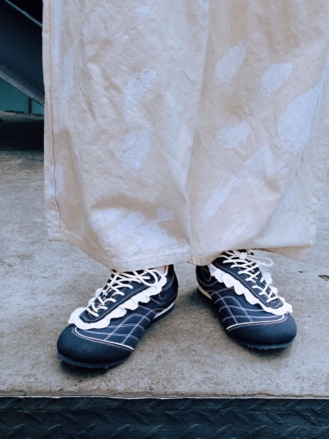 Pair of navy contrast-stitch low-profile trainers worn with off-white wide-leg trousers in a modern streetwear outfit