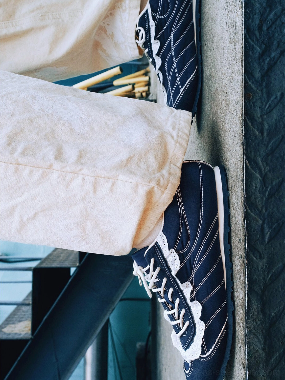Navy contrast-stitch trainers worn with relaxed off-white casual pants in an urban stairwell setting