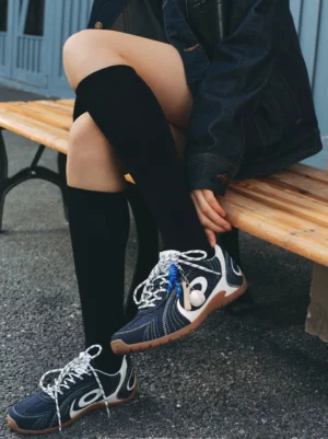 Navy low-profile retro trainers styled with black knee-high socks and dark denim in an outdoor streetwear look