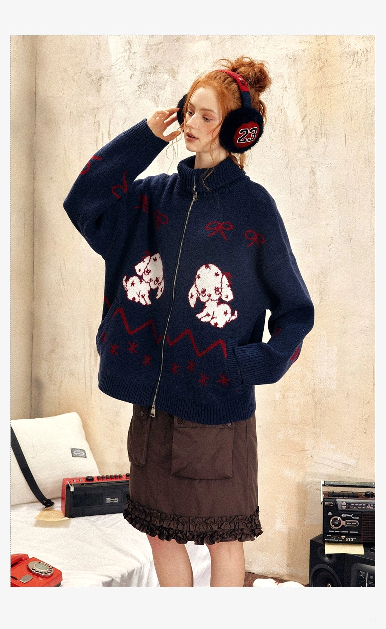 Front three-quarter view of a navy oversized puppy jacquard zip-up sweater with red bows and ribbed edges in a vintage-inspired outfit