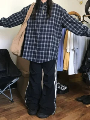 Full front view of a navy plaid button-front flannel shirt styled with black wide-leg track pants in a contemporary streetwear studio outfit