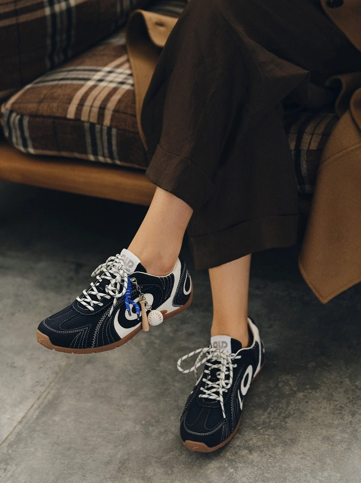 Navy retro trainers with gum soles placed beside a relaxed brown streetwear outfit on a plaid sofa