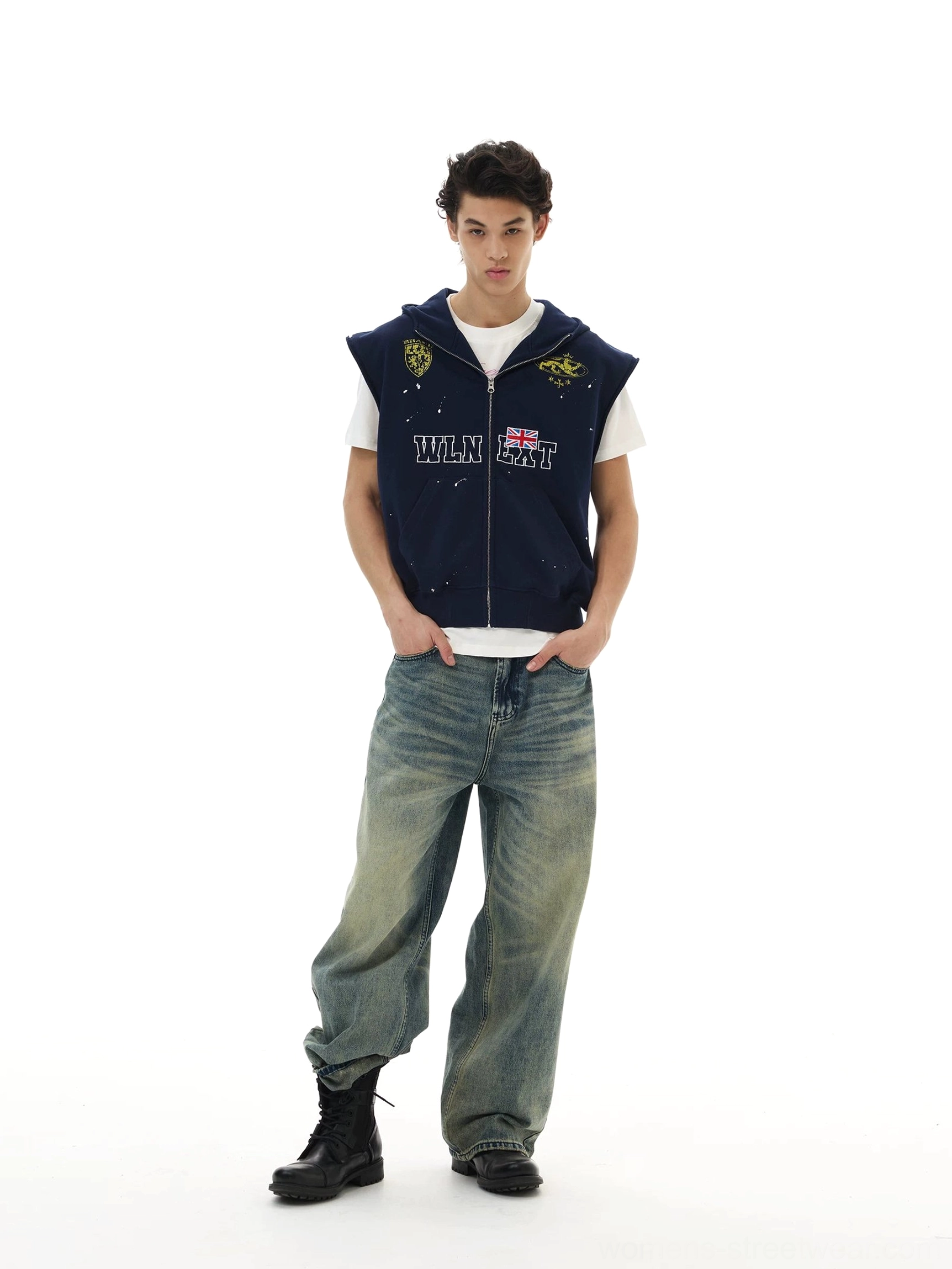Relaxed navy sleeveless zip hoodie vest layered over white T-shirt with distressed denim and workwear boots