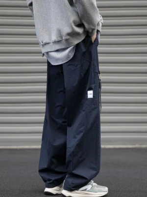 Navy streetwear cargo pants shown from the rear side with adjustable drawstring waist, relaxed wide-leg silhouette, utility pocket, gray layered hoodie, and casual sneakers