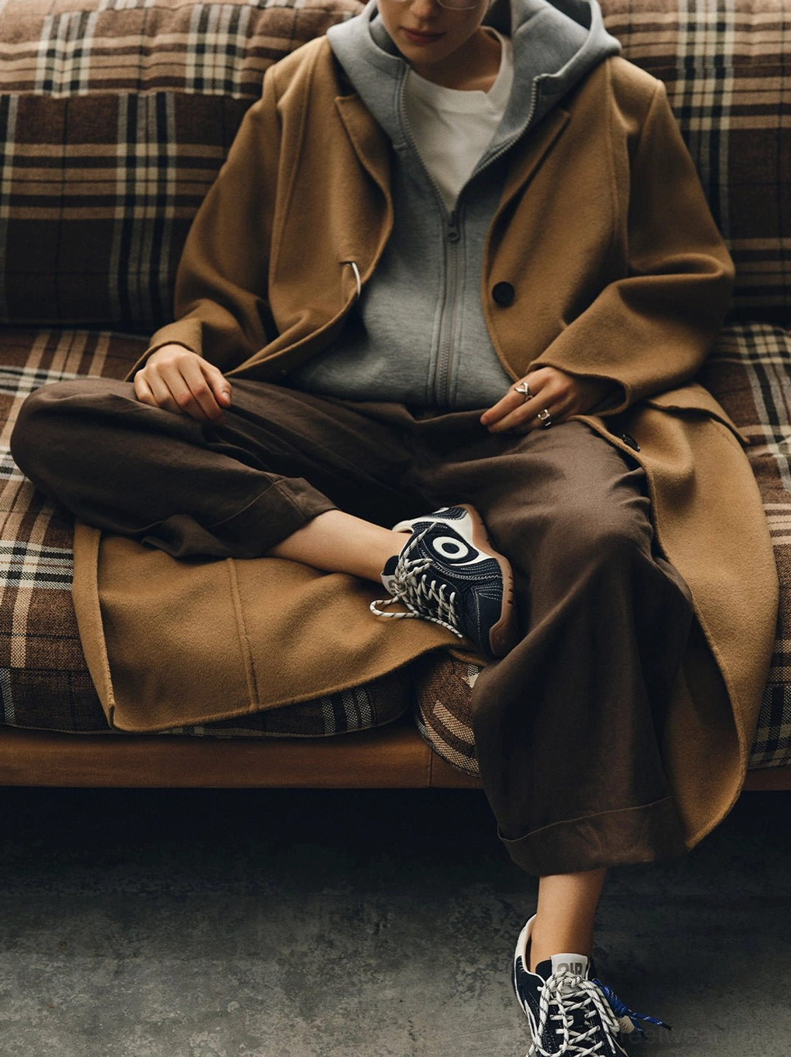 Navy swirl-panel trainer worn with a brown coat, gray hoodie, and relaxed trousers for layered Korean fashion