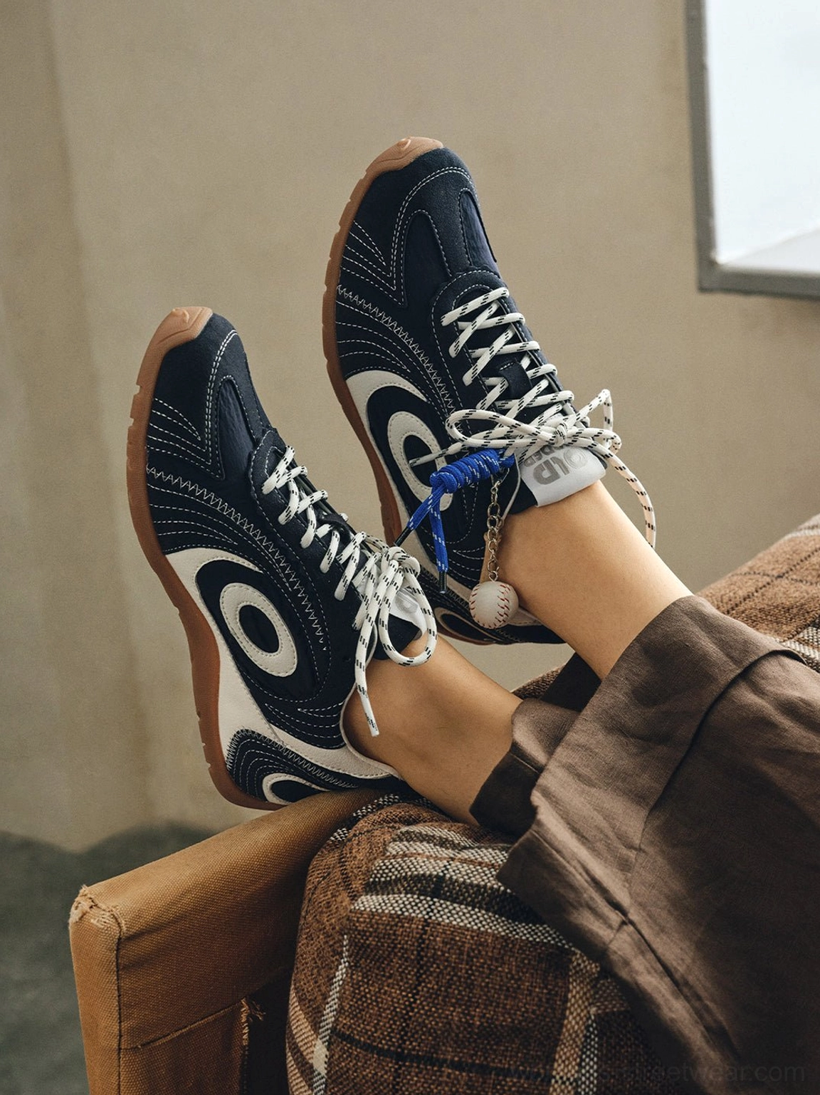 Pair of navy swirl-panel low-profile trainers with white graphic overlays and blue laces styled with brown trousers