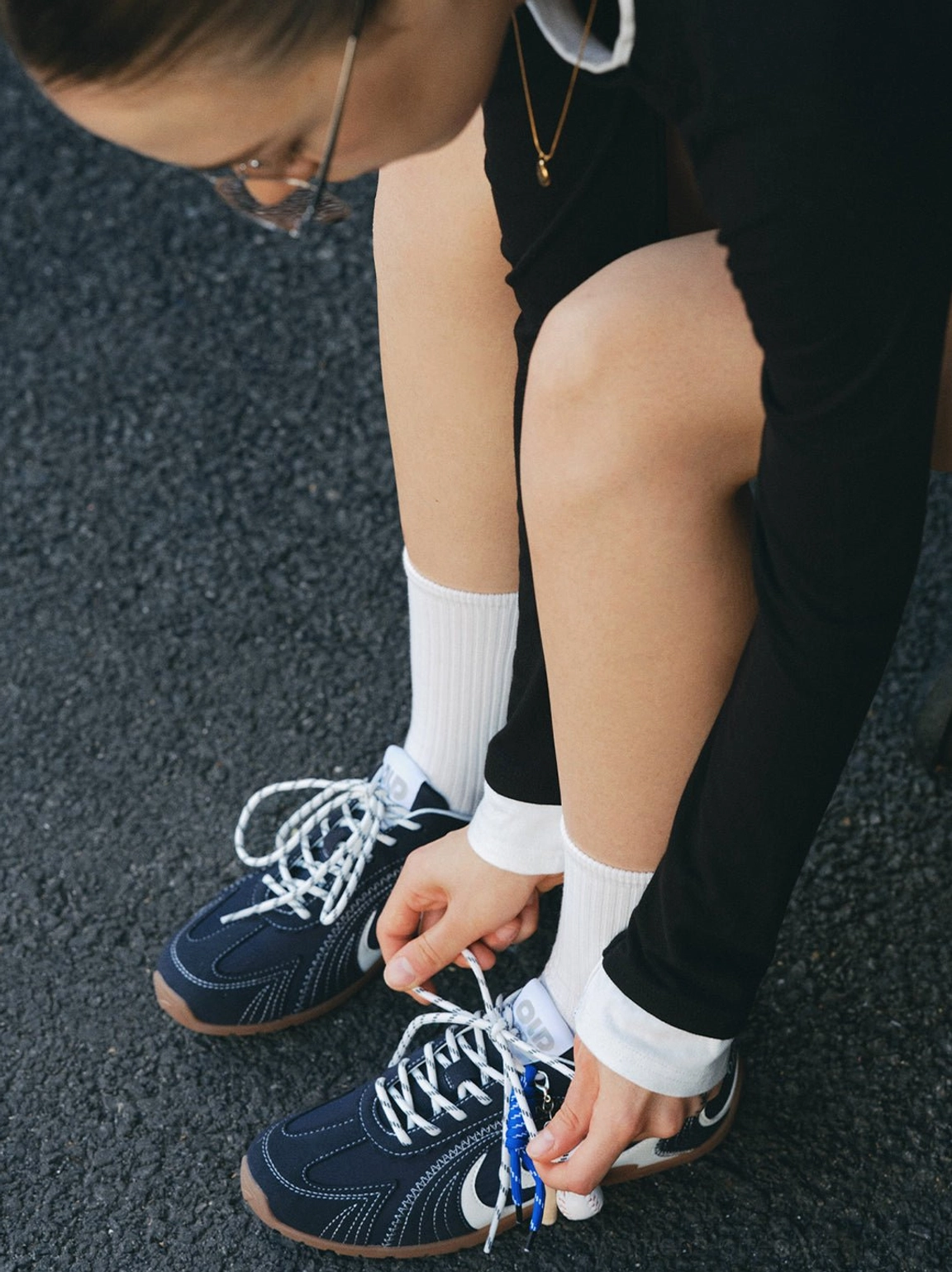 Close-up of navy swirl trainers with blue laces and baseball charm being tied on an outdoor asphalt street
