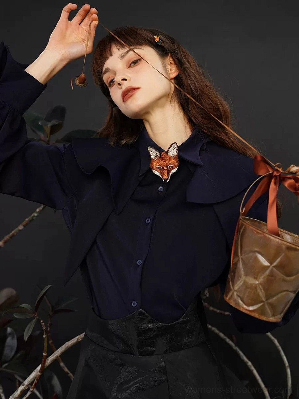 Navy toned cape collar blouse styled with a layered collar, slim waist silhouette, fox brooch accessory, and woven leather handbag