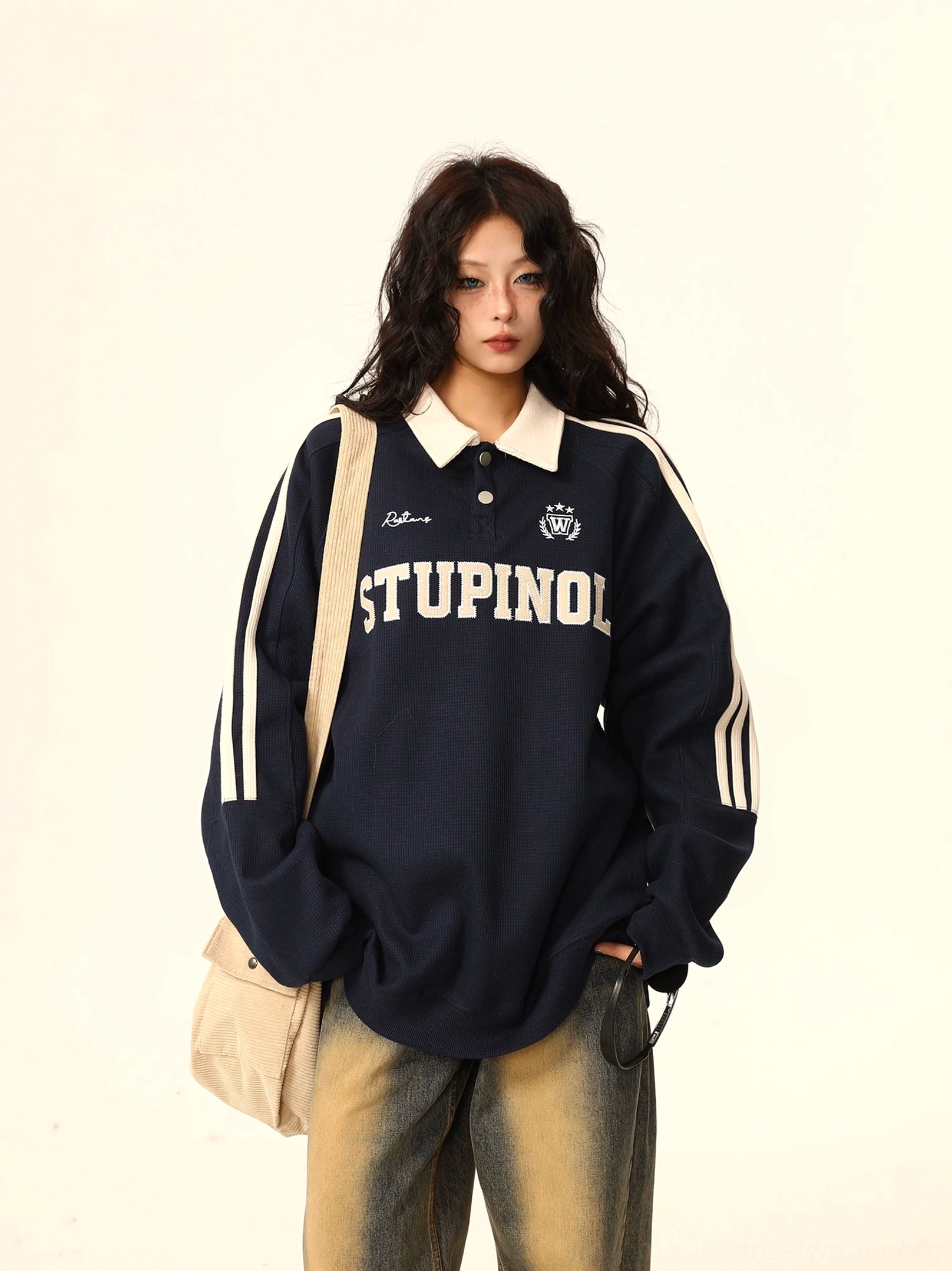 Navy oversized polo collar varsity sweatshirt with white athletic sleeve stripes, embroidered lettering, and crest detail worn with wide-leg jeans