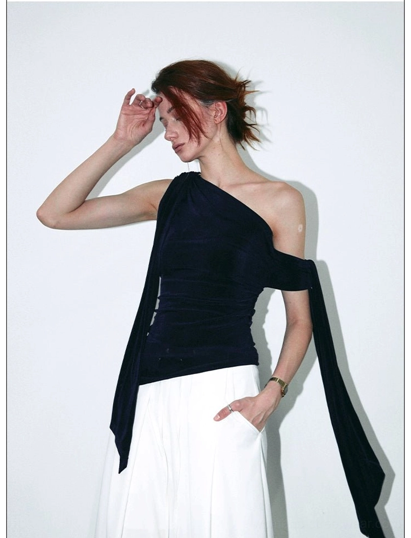 Front three-quarter styling view of a navy velvet one-shoulder draped top with asymmetric hem and modern wide-leg pants