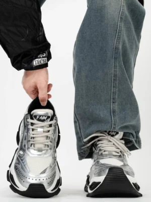 Liquid silver futuristic chunky platform sneakers with metallic mesh upper, black layered sole, and approximately 10cm height lift styled with baggy blue jeans