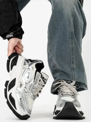 Side profile of futuristic silver chunky streetwear sneakers with black geometric overlays, mesh panels, textured wave sole, and elevated platform design