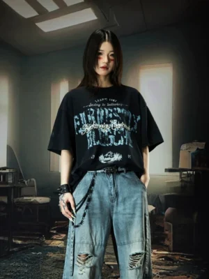 Female model wearing black Nebula Varsity oversized graphic streetwear T-shirt with blue distressed chest print and ripped wide-leg jeans