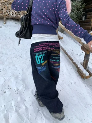 Side rear view of dark blue wide-leg graffiti jeans featuring vibrant multicolor text graphics, styled with a black shoulder bag and casual Korean streetwear layers