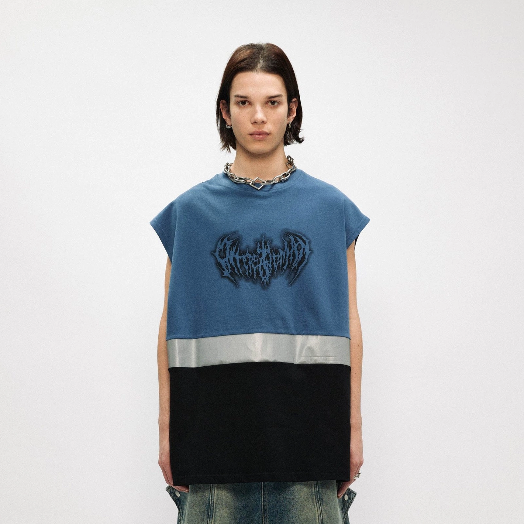 Male model wearing a dusty blue and black oversized gothic graphic tank top with reflective stripe and loose jeans