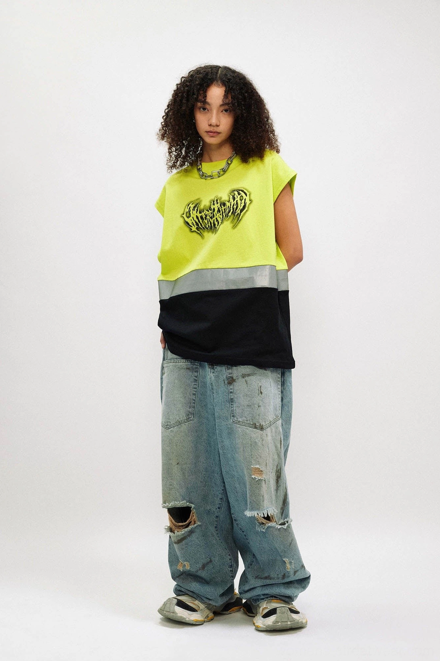 Female model styling an oversized fluorescent lime gothic tank top with ripped loose denim jeans