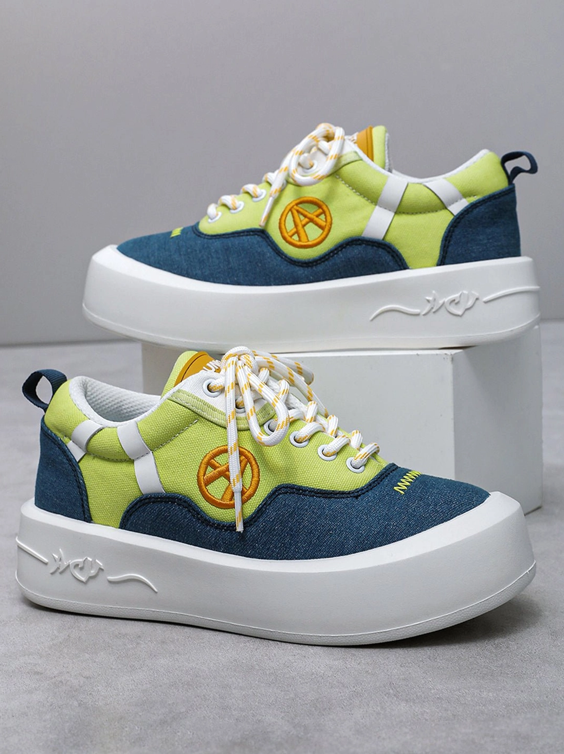 Stacked display of neon colorblock streetwear platform sneakers with orange side patch and thick white sole