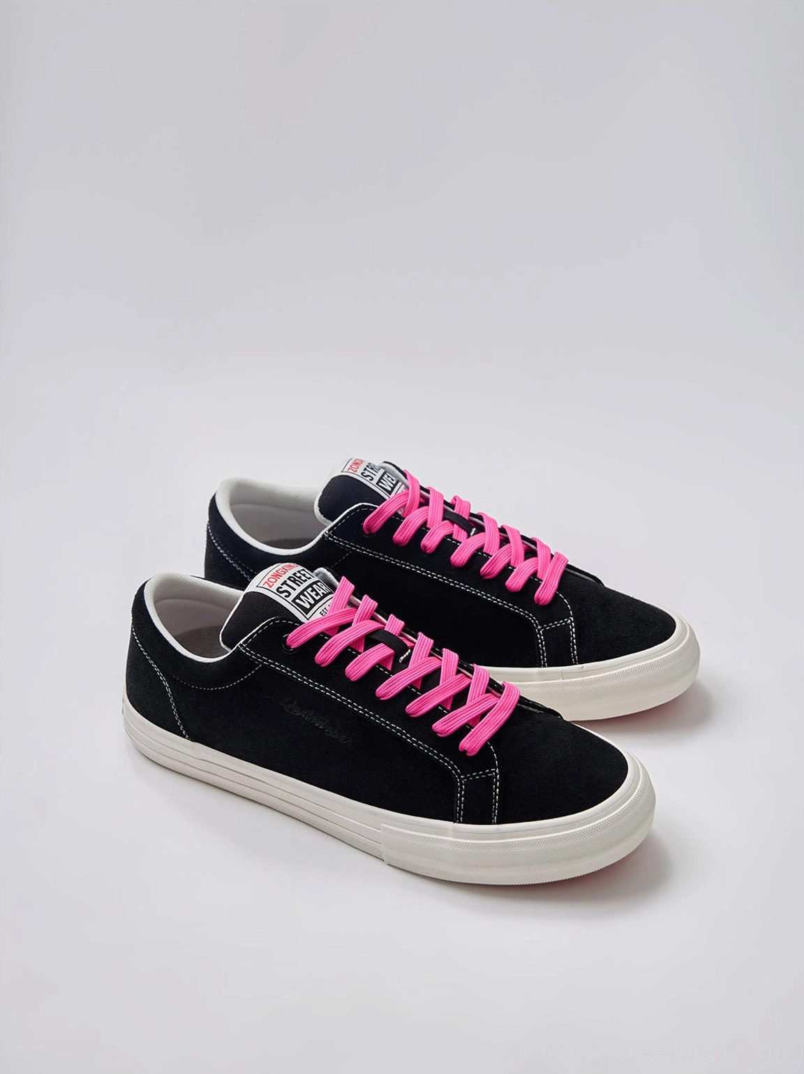 Pair of black suede low-top platform canvas sneakers with neon laces and clean white rubber soles on a light background