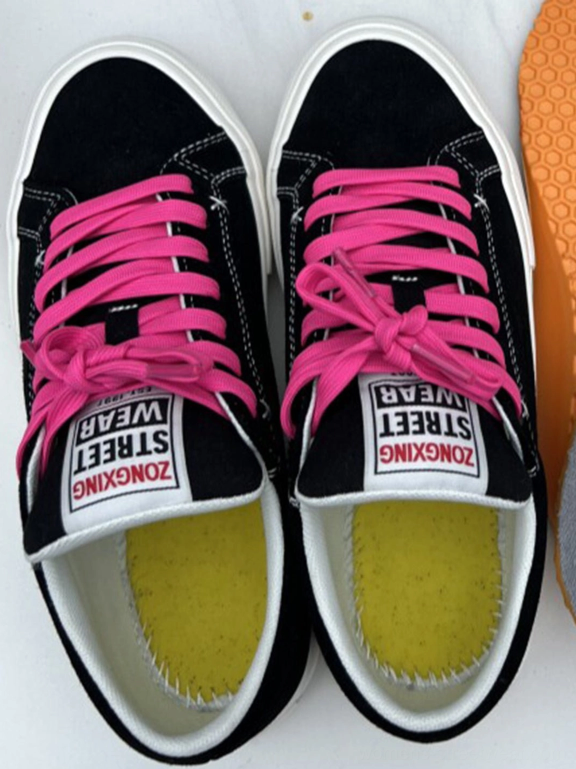 Top view of black suede platform canvas sneakers with neon pink laces, yellow insoles, white stitching, and thick rubber soles