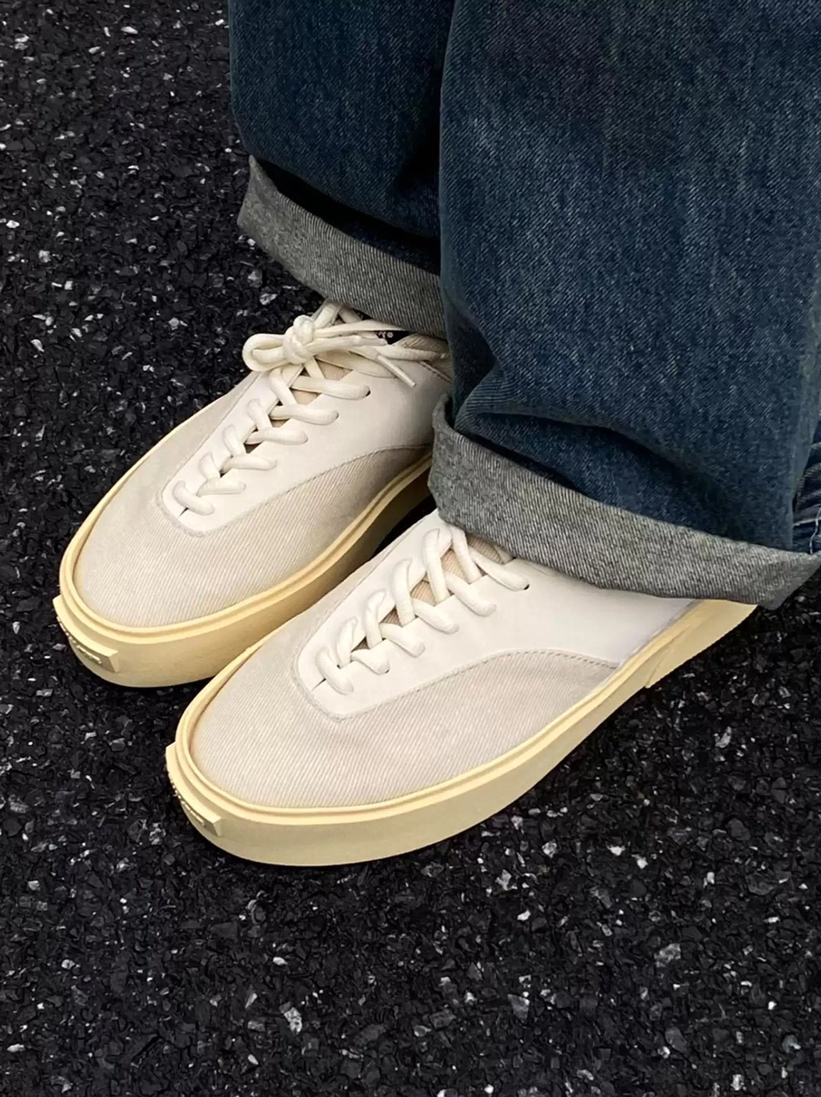 Overhead view of neutral platform canvas sneakers worn with rolled-up denim jeans on dark gravel, highlighting the off-white upper, lace-up design, and chunky cream sole