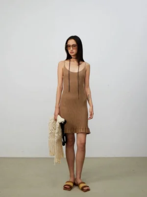 Female model wearing a neutral ribbed knit mini dress and carrying a small woven fringe tote bag with woven slide sandals