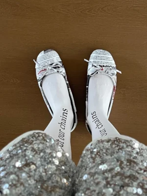 Women's newspaper print ballet flats styled with silver sequined shorts and white typography tights in a streetwear outfit