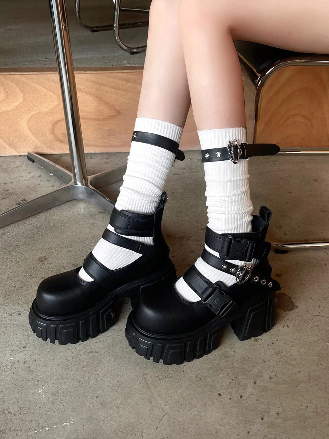 Black buckled platform boots worn with ribbed white socks in a cafe outfit, showing chunky lug soles and punk streetwear styling