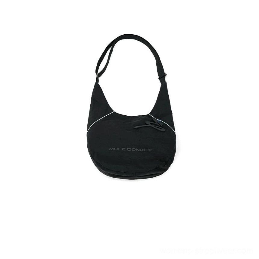 Back view of black utility sling hobo crossbody bag with reflective side trim hidden zippered pocket and adjustable strap