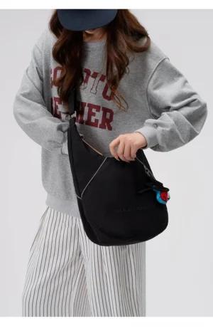 Female model wearing a black utility sling hobo crossbody bag with reflective trim and adjustable strap in a casual streetwear outfit