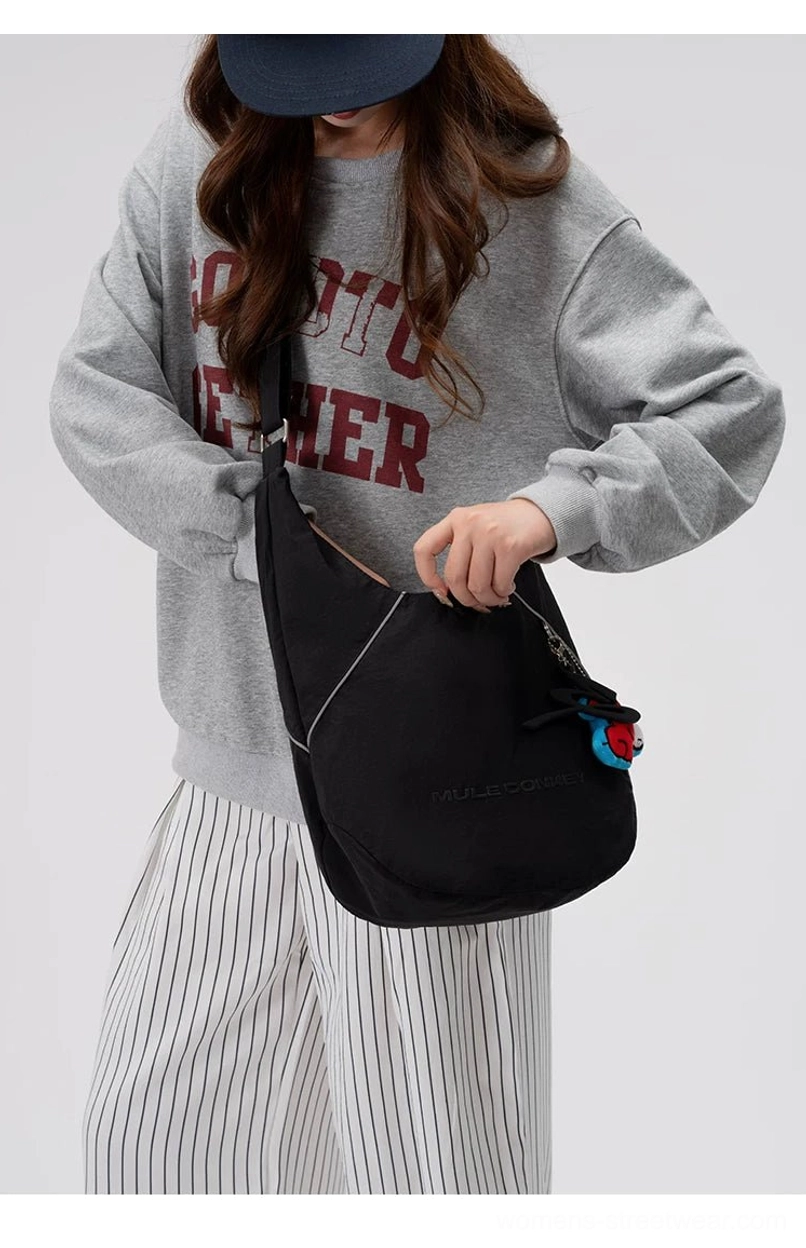 Female model wearing a black utility sling hobo crossbody bag with reflective trim and adjustable strap in a casual streetwear outfit