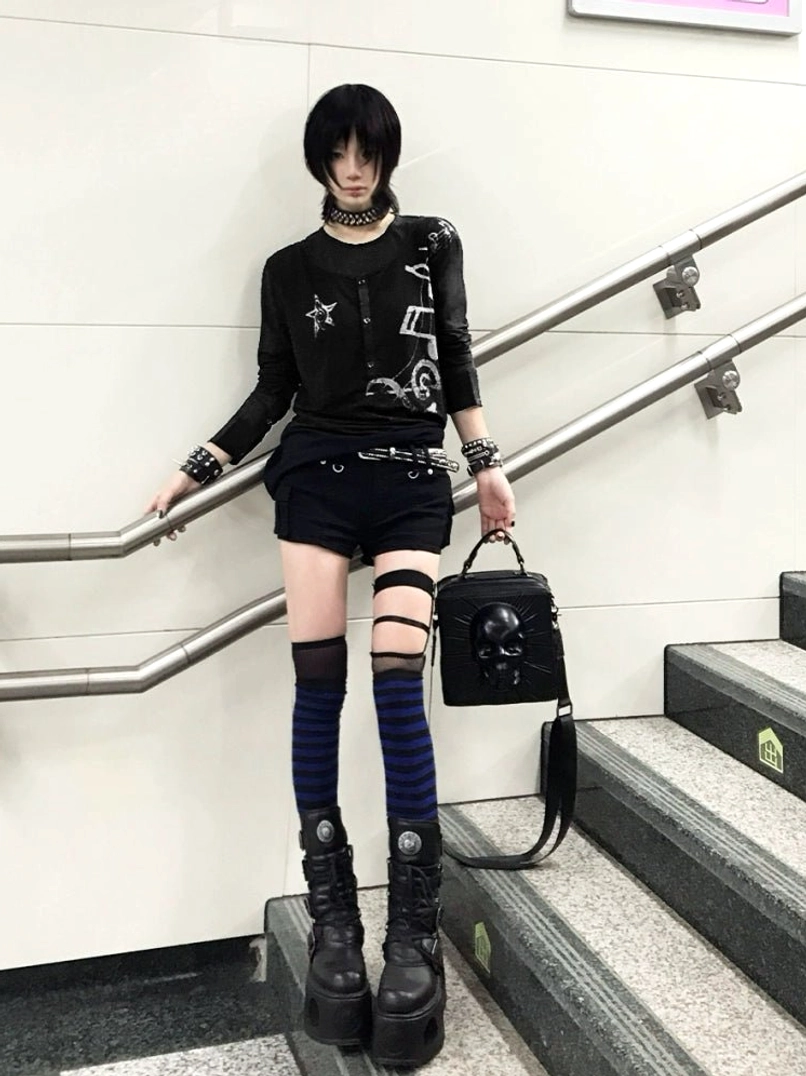 Black goth layered long sleeve music graphic top styled with platform boots in subway stairwell