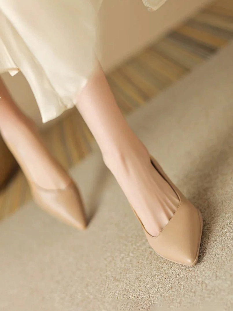 Nude pointed-toe kitten heel pumps with smooth matte leather finish styled with a cream ruffled skirt