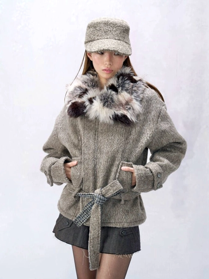 Oat ash wool blend streetwear coat with oversized mixed tone faux fur shawl collar, plaid tie belt, dropped shoulders, tabbed cuffs, slant pockets, and boxy hip length silhouette styled with a newsboy cap and dark mini skirt