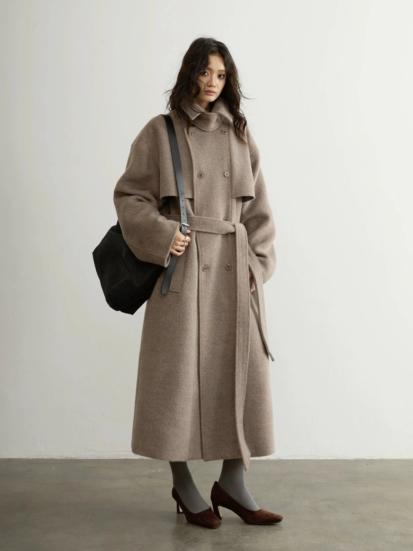 Oatmeal belted double-breasted wool blend long coat styled with shoulder bag in studio three-quarter view