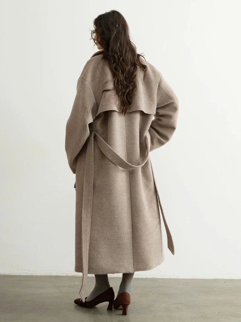 Back view of oatmeal full-length oversized belted wool blend trench coat worn in minimalist studio