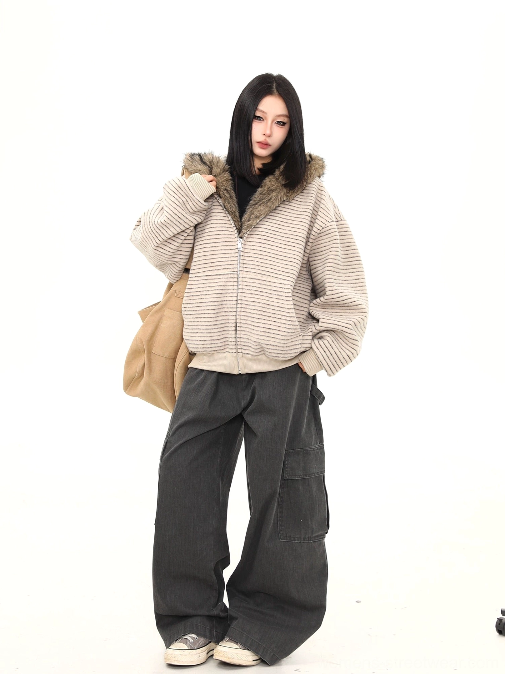 Side view of an oatmeal striped faux fur hooded streetwear jacket styled with wide cargo pants canvas sneakers and tote bag