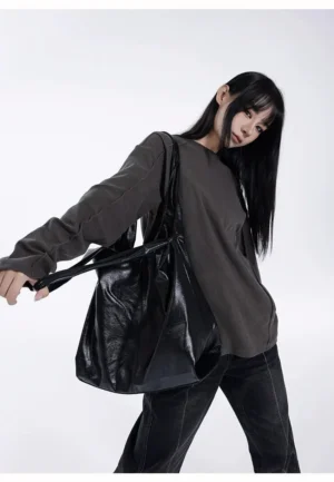 Black glossy faux leather slouch hobo tote bag side view worn with oversized gray sweatshirt and black jeans