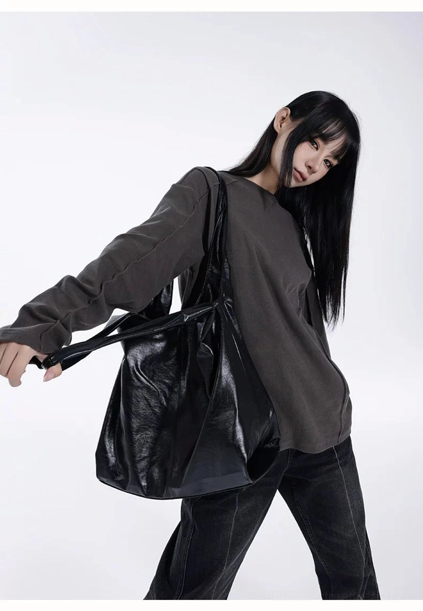 Black glossy faux leather slouch hobo tote bag side view worn with oversized gray sweatshirt and black jeans