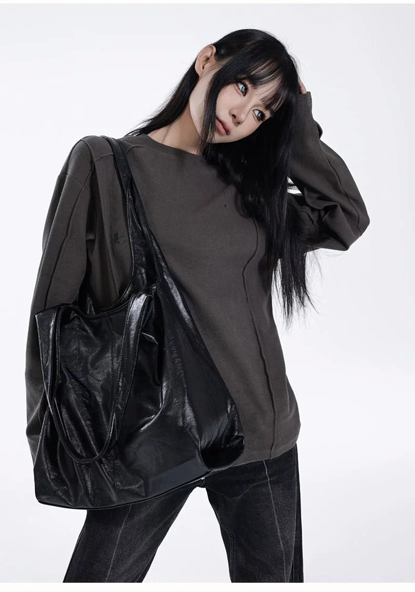 Obsidian glossy black slouch hobo tote bag worn on shoulder with dark gray streetwear outfit front view