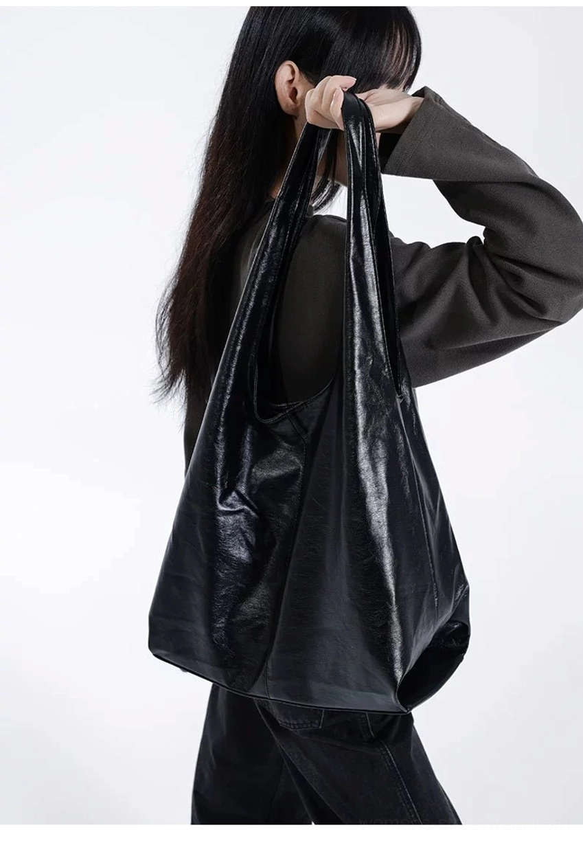 Front close-up of oversized black glossy crinkled leather-look slouch hobo tote worn on shoulder