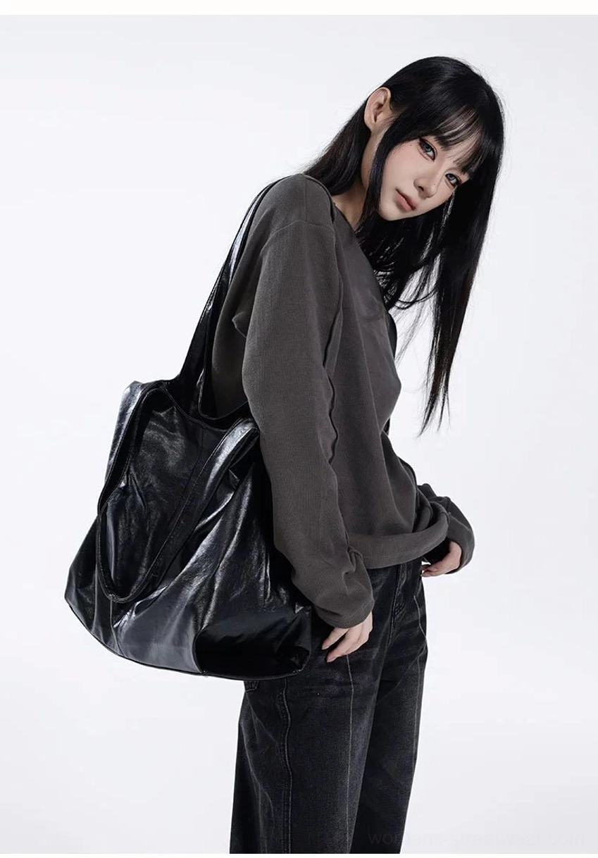 Oversized black faux leather hobo tote naturally draped at hip for relaxed Korean streetwear styling