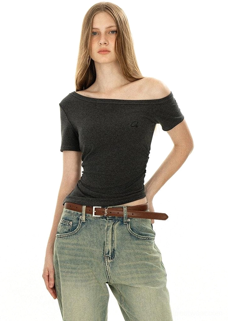 Off-shoulder dark grey minimalist tee with boat neckline and embroidered logo worn with vintage washed jeans and brown leather belt front view streetwear styling