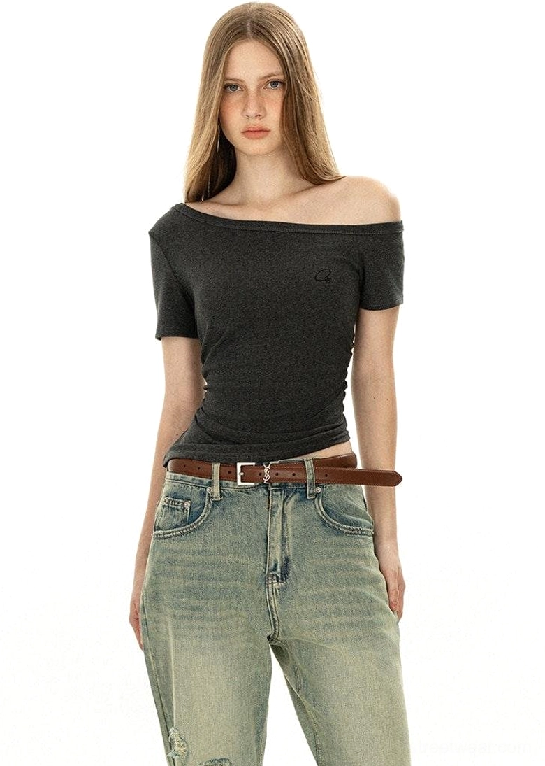 Front half-body off-shoulder dark grey minimalist tee with boat neckline embroidered logo and brown leather belt styling vintage aesthetic