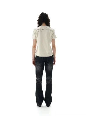 Back view of an off white graphic short sleeve tee showing subtle shoulder script detail with dark flared jeans