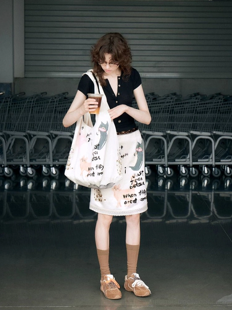 Off-white cat graffiti hobo tote bag styled with a black cropped top, printed skirt, retro sneakers, and casual streetwear outfit