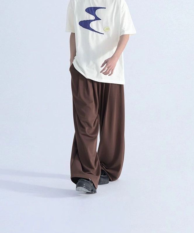 Side three-quarter view of an off-white relaxed fit contrast graphic tee with navy wavy front patch design, brown trousers, and black casual sneakers